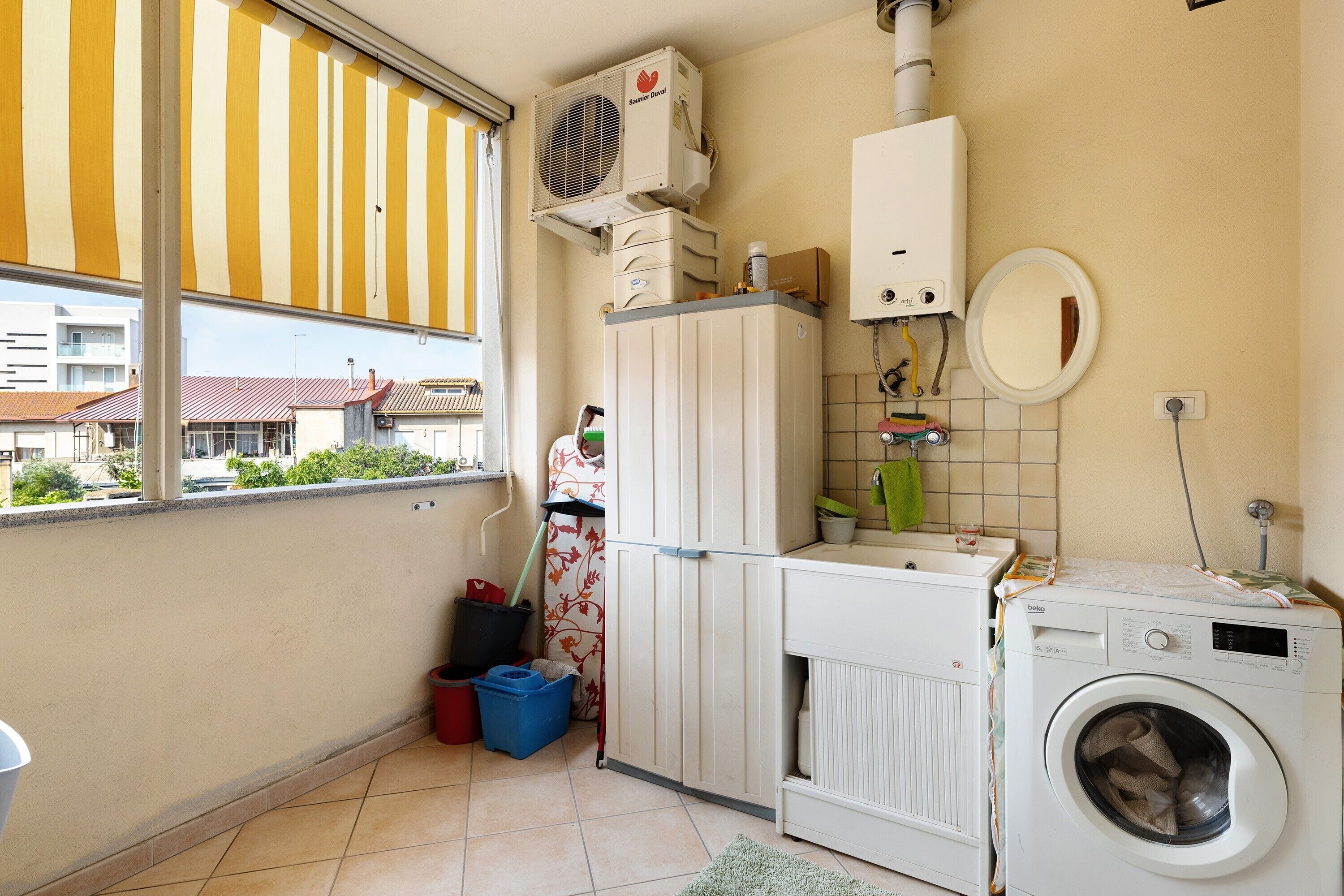 A laundry room with a washing machine, a dryer, a radiator, and a window with a striped blind.