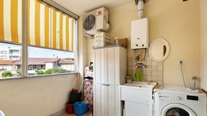 A laundry room with a washing machine, a dryer, a radiator, and a window with a striped blind.