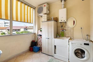 Une buanderie équipée d’un lave-linge, d’un sèche-linge, d’un radiateur et d’une fenêtre avec un store à rayures.