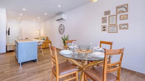 A modern dining area with a round glass table, wooden chairs, and a central island with a blue countertop. - Qala Tranquil Escape - Stylish with Terrace & AC (Qala)