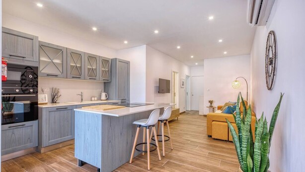 A modern kitchen with grey cabinets, a central island, and a dining area with a sofa and chairs. - Qala Tranquil Escape - Stylish with Terrace & AC (Qala)