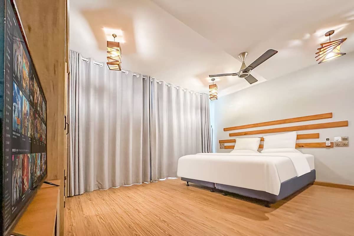 A modern hotel room with a large bed, ceiling fan, and a wall-mounted TV.