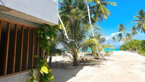 A beachfront property with a white building, palm trees, and a sandy path leading to the ocean. - WhiteSand (Himandhoo)