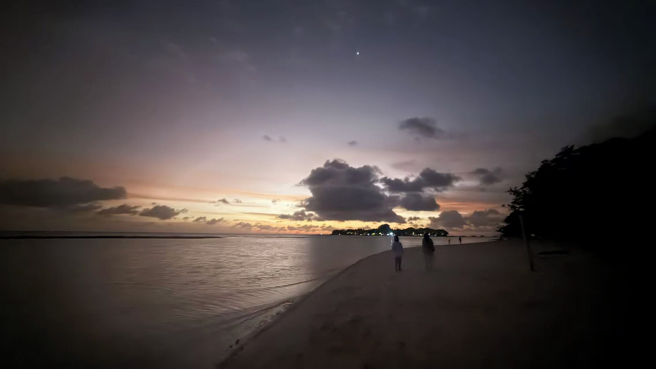 A beach with a calm sea and a sunset.