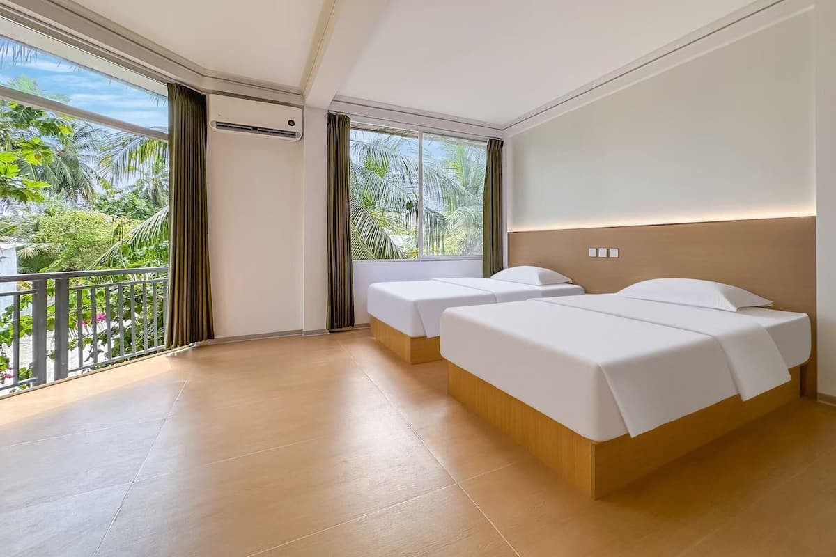 A hotel room with two beds, a balcony, and large windows offering a view of greenery.