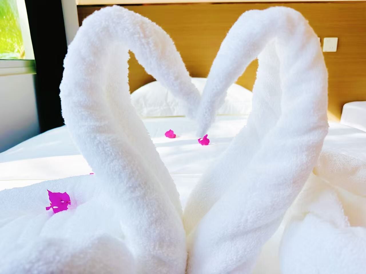 A bed with a white blanket and two towels arranged in a heart shape.