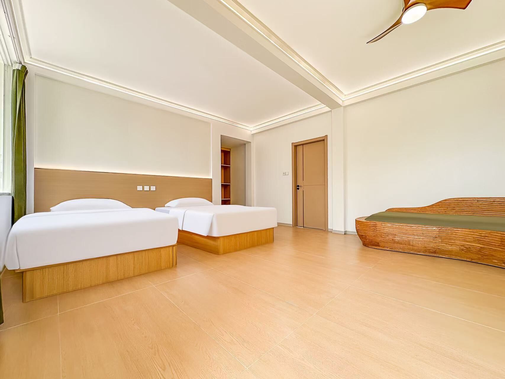 Een hotelkamer met twee eenpersoonsbedden, een slaapbank, een houten vloer en een deur naar een badkamer.