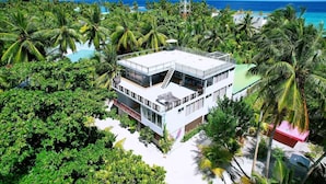 A modern multi-story building surrounded by lush greenery and a clear view of the ocean. - WhiteSand (Himandhoo)
