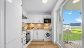 A modern kitchen with white cabinets, a built-in oven, microwave, and washing machine.