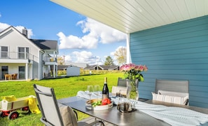 An outdoor patio with a table set for two, featuring a bottle of wine, glasses, and a bowl of fruit.