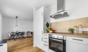 A modern kitchen with white cabinets, a Bosch oven, and a dining area with a table and chairs.