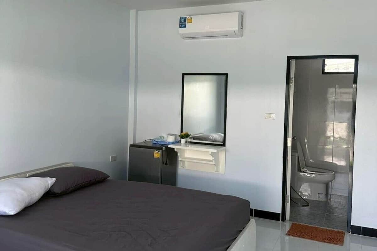 A modern hotel room with a large bed, a small desk with a mirror, an air conditioning unit, and a bathroom with a toilet and shower.