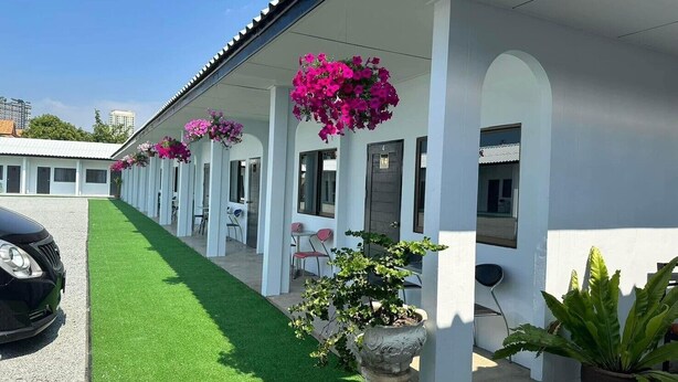 A row of white rooms with individual doors, a car parked in front, and a green artificial lawn. - 17 Garden  (Pattaya)
