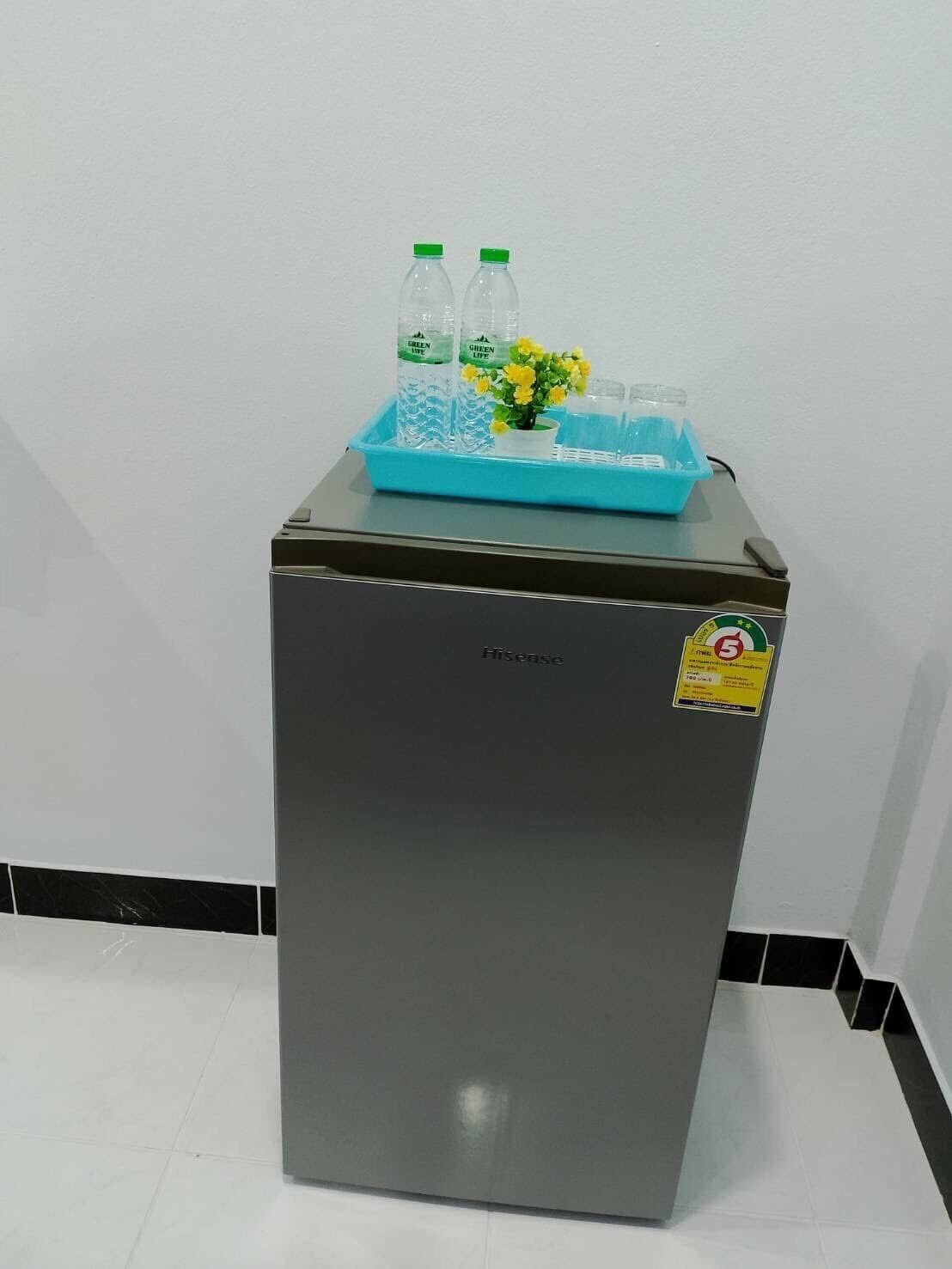 A compact refrigerator with a sticker indicating a 5-star rating, placed on a tiled floor against a plain wall.