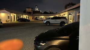 A parking area with several cars, a building with a flat roof, and a tall illuminated structure in the background. - 17 Garden  (Pattaya)