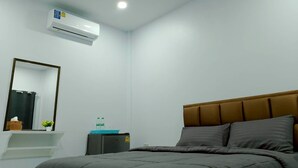 A hotel room with a bed, a bedside table, a mirror, an air conditioning unit, and a small cabinet. - 17 Garden  (Pattaya)