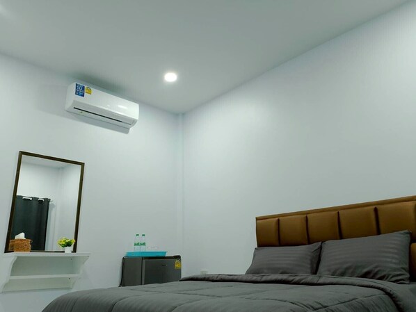 A hotel room with a bed, a bedside table, a mirror, an air conditioning unit, and a small cabinet. - 17 Garden (Pattaya)