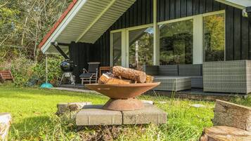 A modern outdoor seating area with a fire pit, surrounded by greenery and a wooden deck.