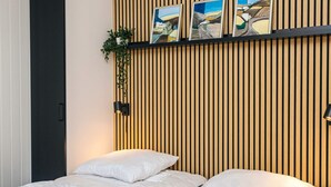 Ein Hotelzimmer mit einer Wand aus Holzlatten, einem Bett mit weißer Bettwäsche und einem kleinen Regal mit gerahmten Bildern und einer Pflanze.