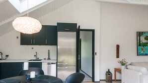 Eine moderne Küche mit dunklen Schränken, einem Edelstahlkühlschrank und einem Essbereich mit rundem Tisch und Stühlen.