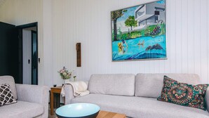 Ein Wohnzimmer mit grauem Sofa, einem Holztisch und einem Gemälde eines Schwimmbeckens.