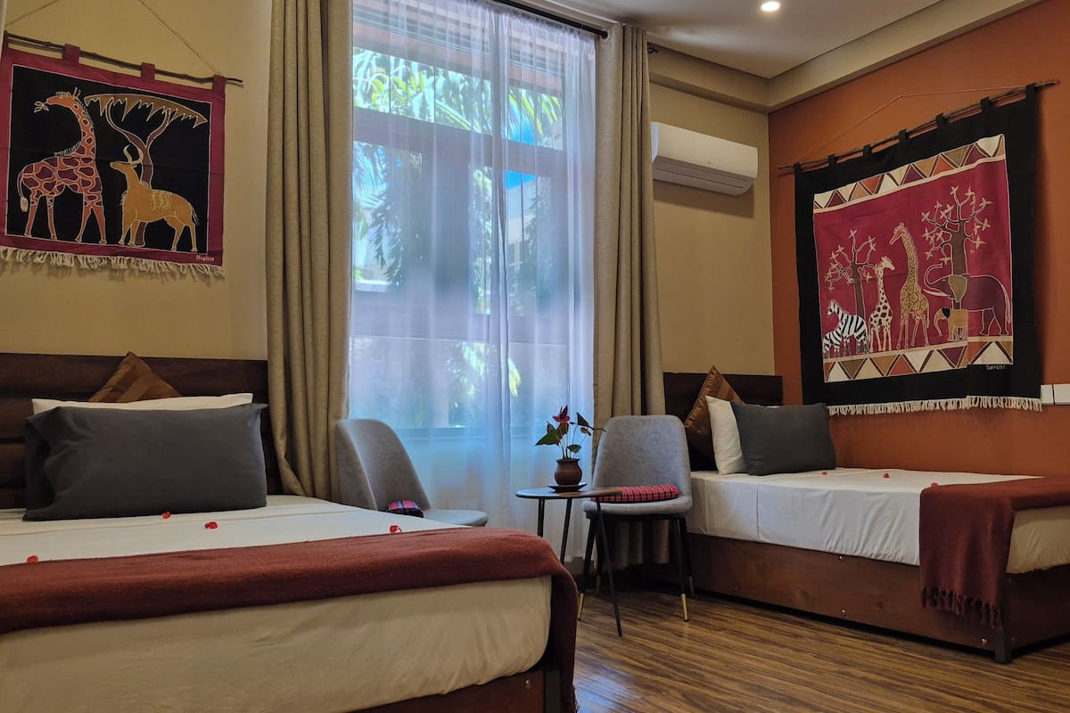 A hotel room with two beds, a small table with a vase, a chair, and a large window with curtains.