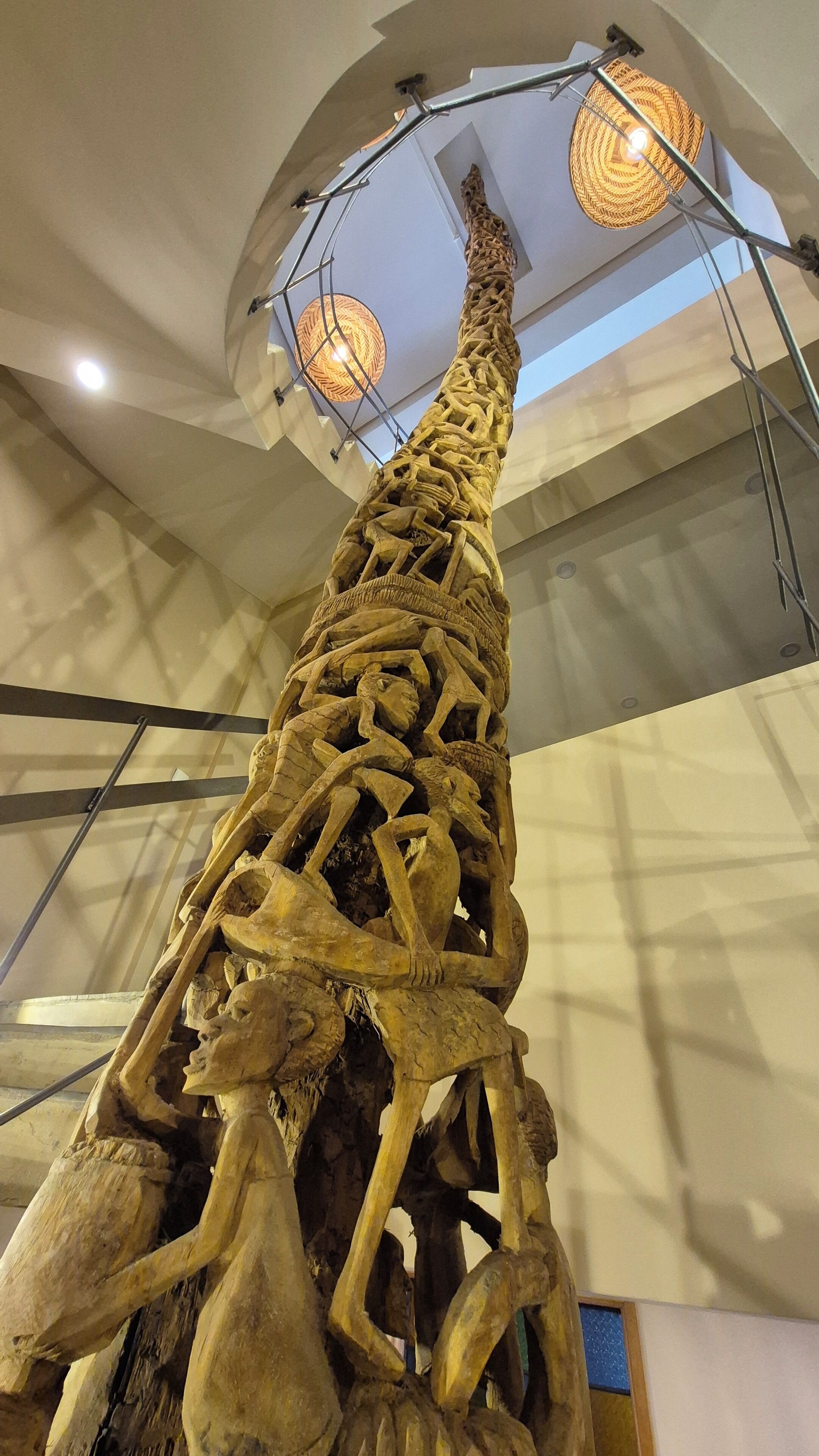 A large, intricately carved dinosaur skeleton displayed indoors, with a high ceiling and modern lighting fixtures.