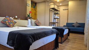 Une chambre d’hôtel avec deux lits, un canapé, une armoire en bois et une étagère avec des serviettes.