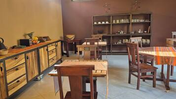 Una habitación acogedora y bien iluminada con muebles de madera, que incluyen una mesa de comedor con sillas, una mesita auxiliar y un aparador con cajones. Hay una estantería con varios objetos, y una escultura decorativa en la pared.