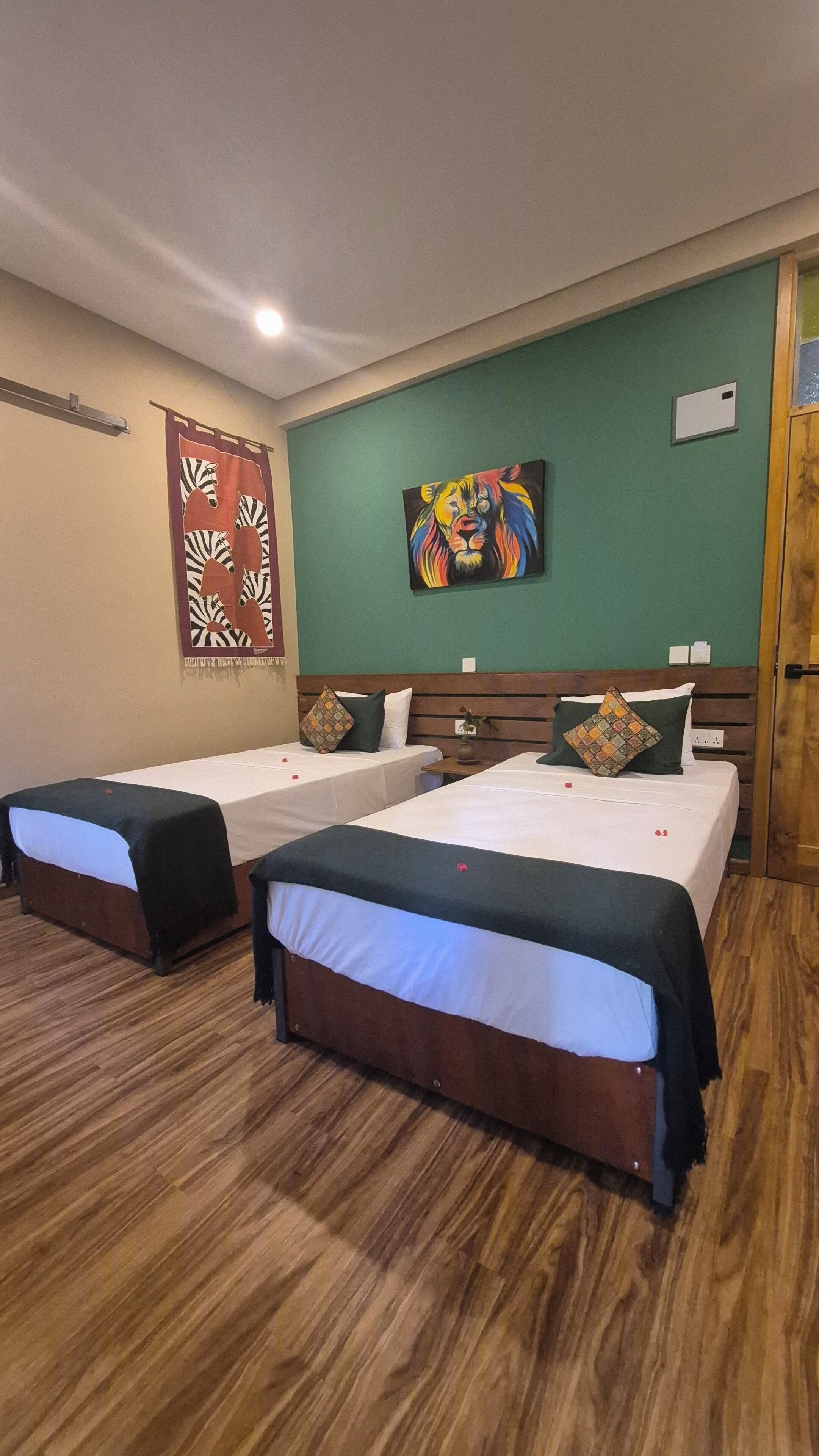 A hotel room with two single beds, a wooden headboard, a green accent wall, and a zebra-themed curtain.
