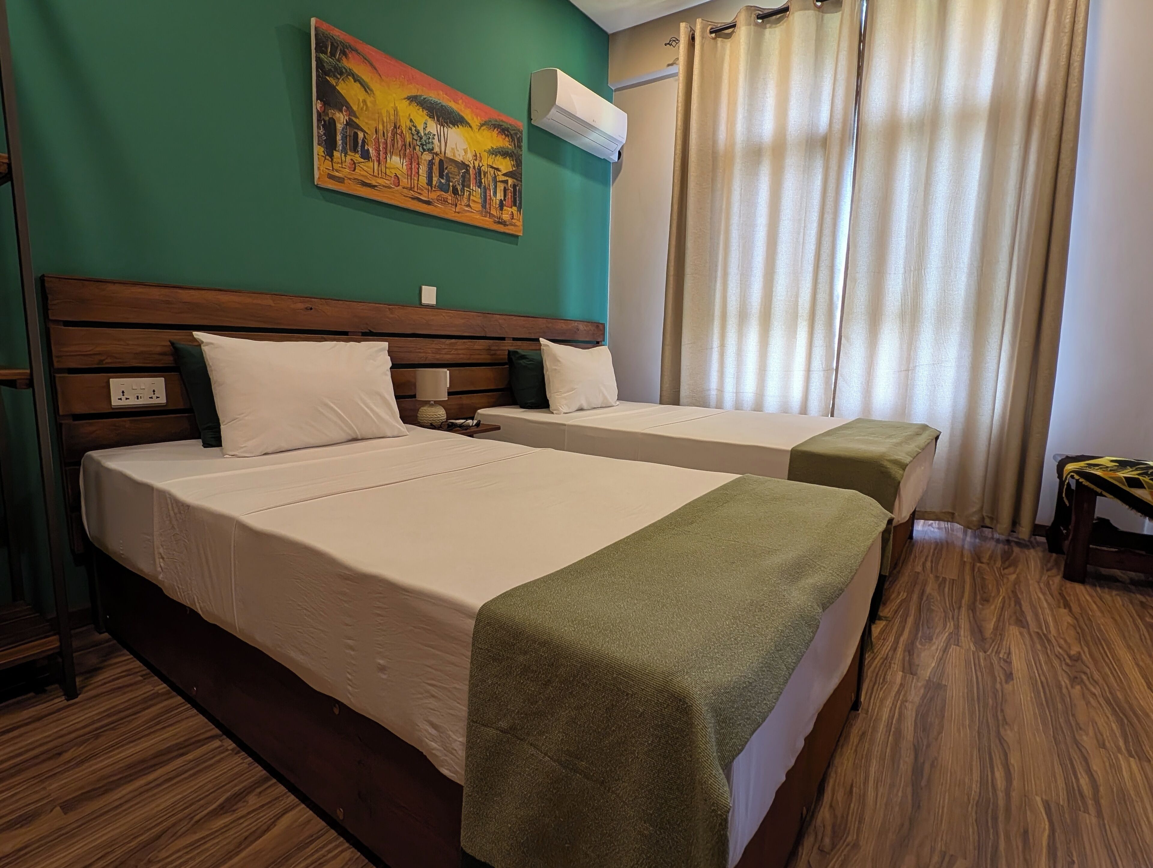 Habitación de hotel con dos camas, cabecero de madera, un cuadro en la pared y una ventana con cortinas.