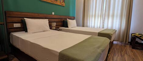 Habitación de hotel con dos camas, cabecero de madera, un cuadro en la pared y una ventana con cortinas.