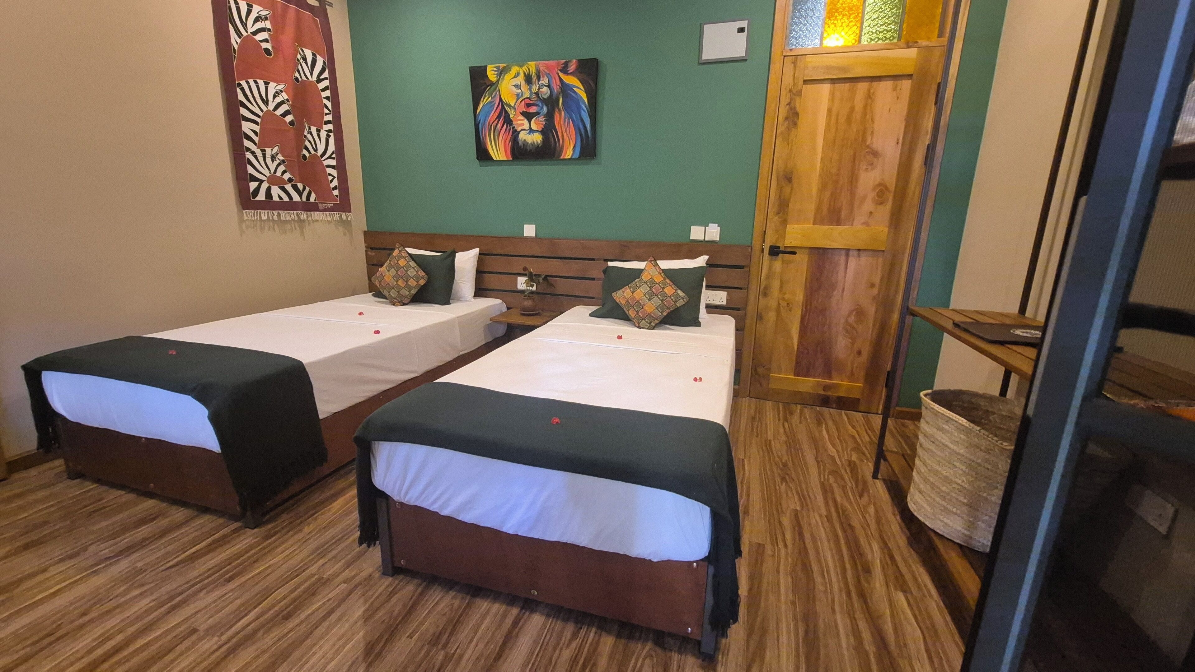 Una habitación con dos camas individuales, una puerta de madera, un cuadro colorido y un adorno en la pared con estampado de cebra.