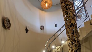 Una escalera de caracol con escalones de piedra y barandilla de metal, rodeada de adornos murales y una lámpara de fibra.