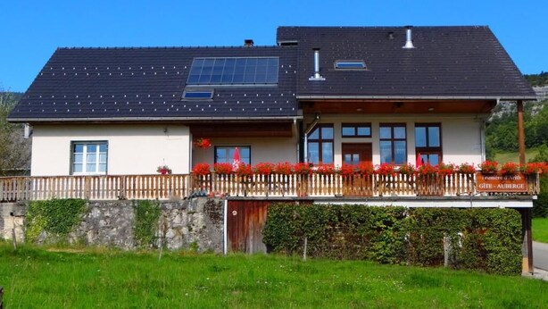 Ein zweistöckiges Haus mit geneigtem Dach, Solaranlagen und einem Holzzaun mit roten Blumen.