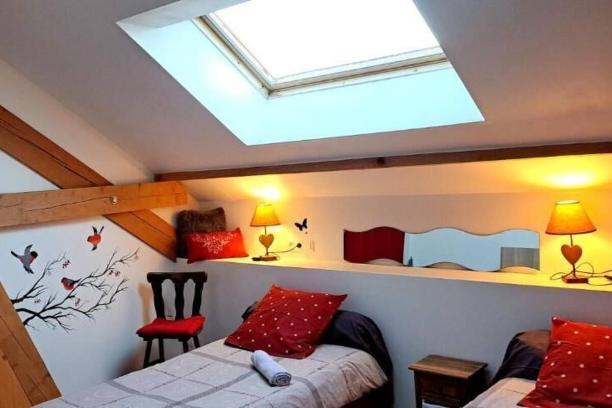A bedroom with a skylight, a bed with red pillows, a chair, and wall decorations.