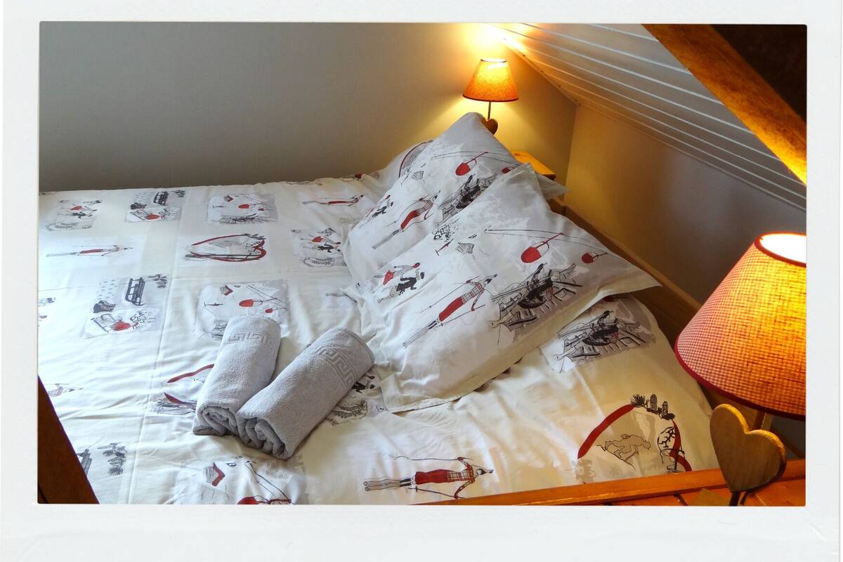 A neatly made bed with white bedding and red and black illustrations, a heart-shaped pillow, and a bedside lamp.