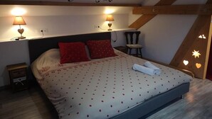 Ein Schlafzimmer mit einem Bett, zwei Nachttischlampen, einem hölzernen Kopfteil, einem kleinen Stuhl und einer Wanddekoration.