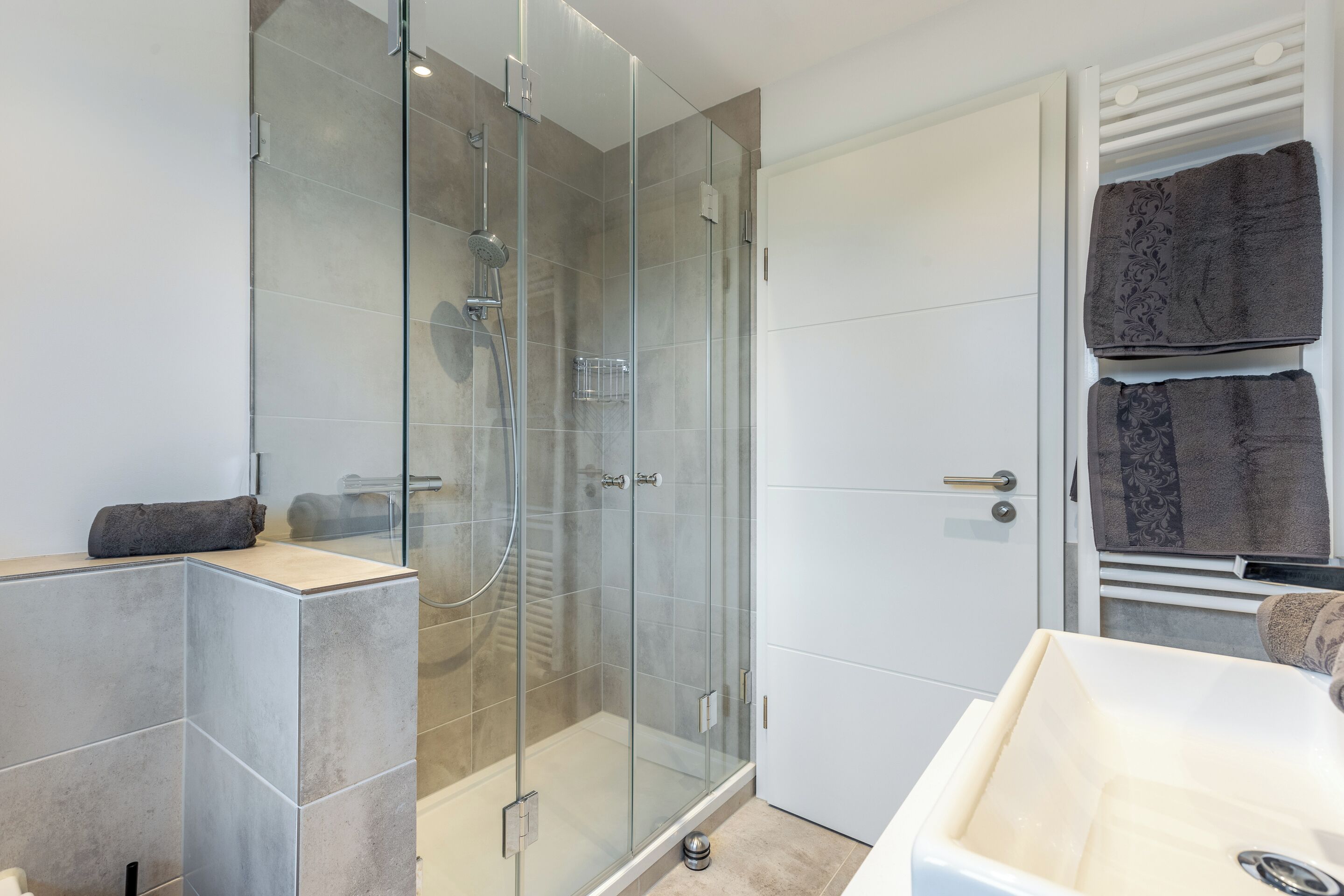 A modern bathroom with a glass-enclosed shower, a white sink, and a towel rack with folded towels.