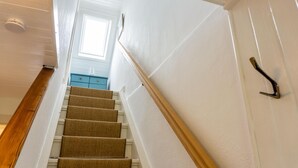 Un escalier avec des marches en bois et une rampe, menant à une pièce où se trouve une commode bleue et une fenêtre.