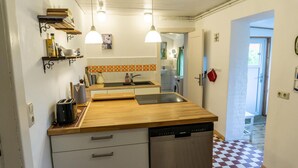 Une cuisine compacte dotée d’un plan de travail en bois, de deux luminaires suspendus, d’un lave-vaisselle et d’un crédence carrelée.