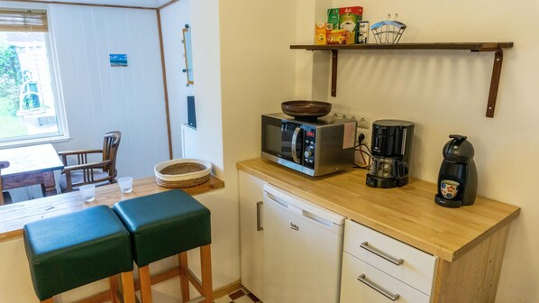Une petite cuisine équipée d’un four à micro-ondes, d’une machine à café et d’une étagère contenant des produits alimentaires.