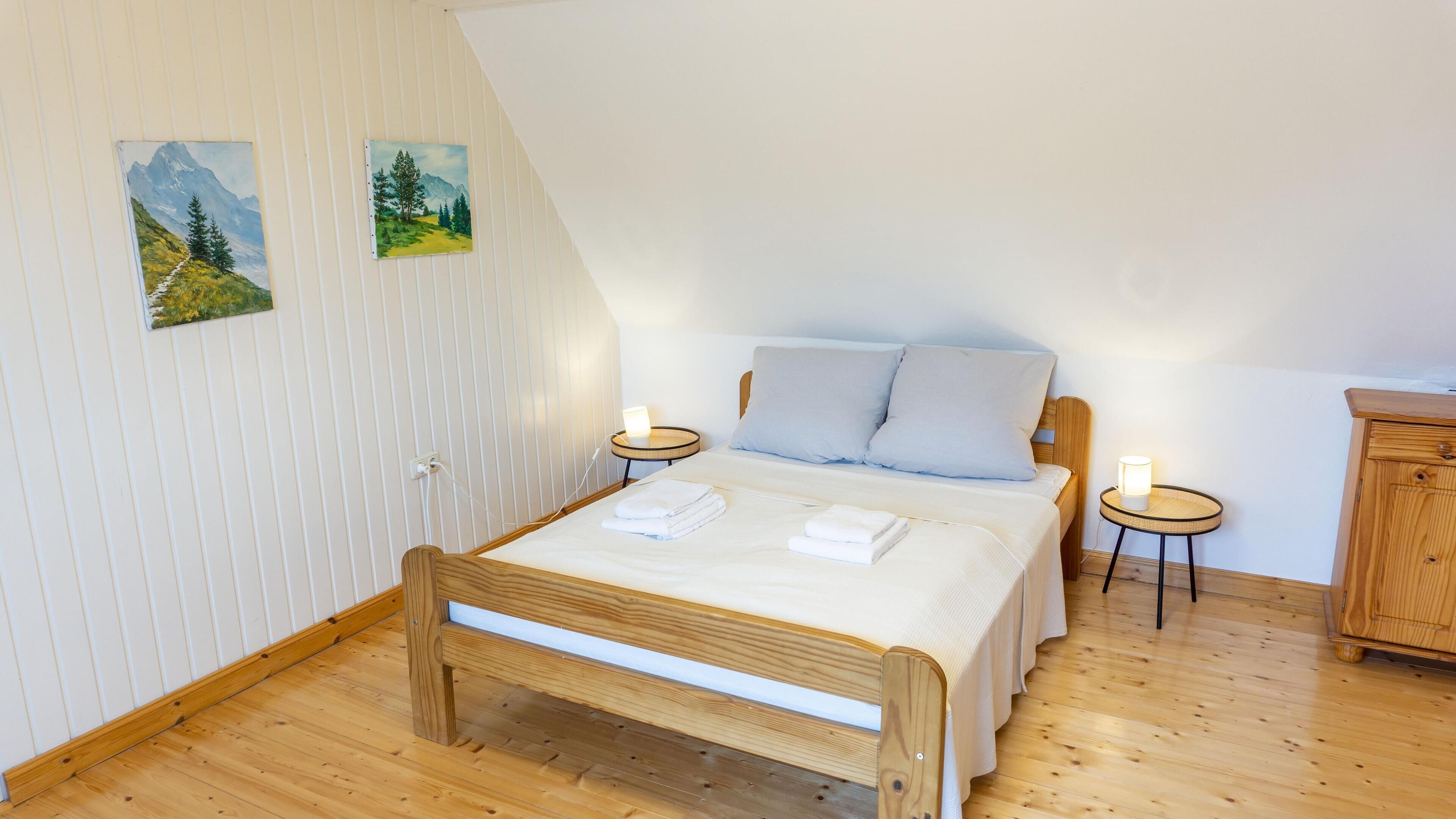 Ein Schlafzimmer mit einem hölzernen Bett, zwei Nachttischen mit Lampen, einem Holzschrank und zwei Bildern an der Wand.