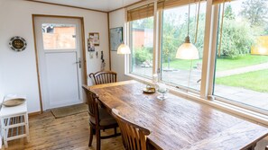 Un coin repas comprenant une table en bois, des chaises, un petit tabouret et une fenêtre donnant sur un jardin.