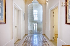 A corridor with a tiled floor, white walls, and a staircase leading to a balcony.