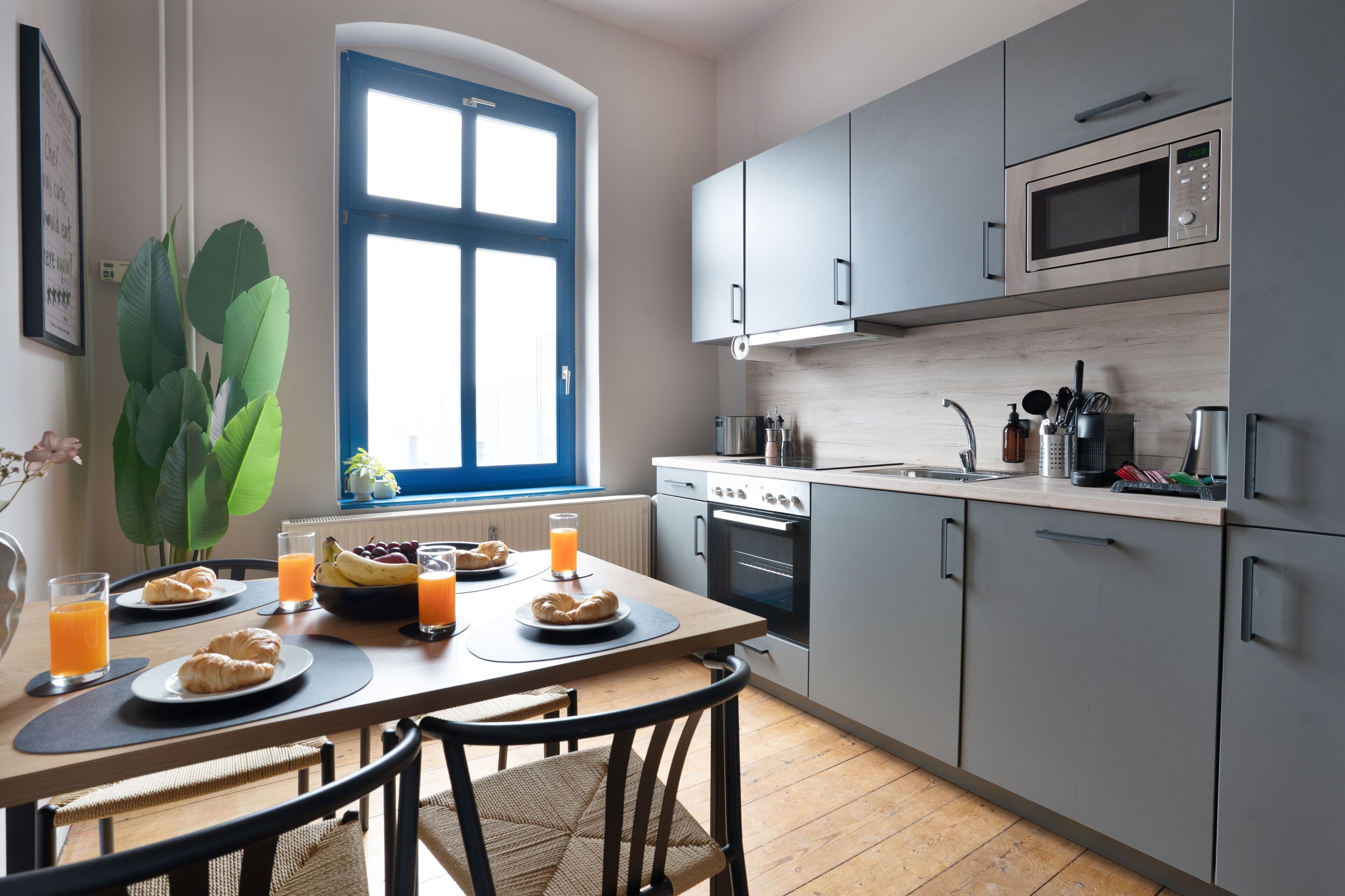 A modern kitchen with grey cabinets, a microwave, and a dining area with a table set for breakfast.