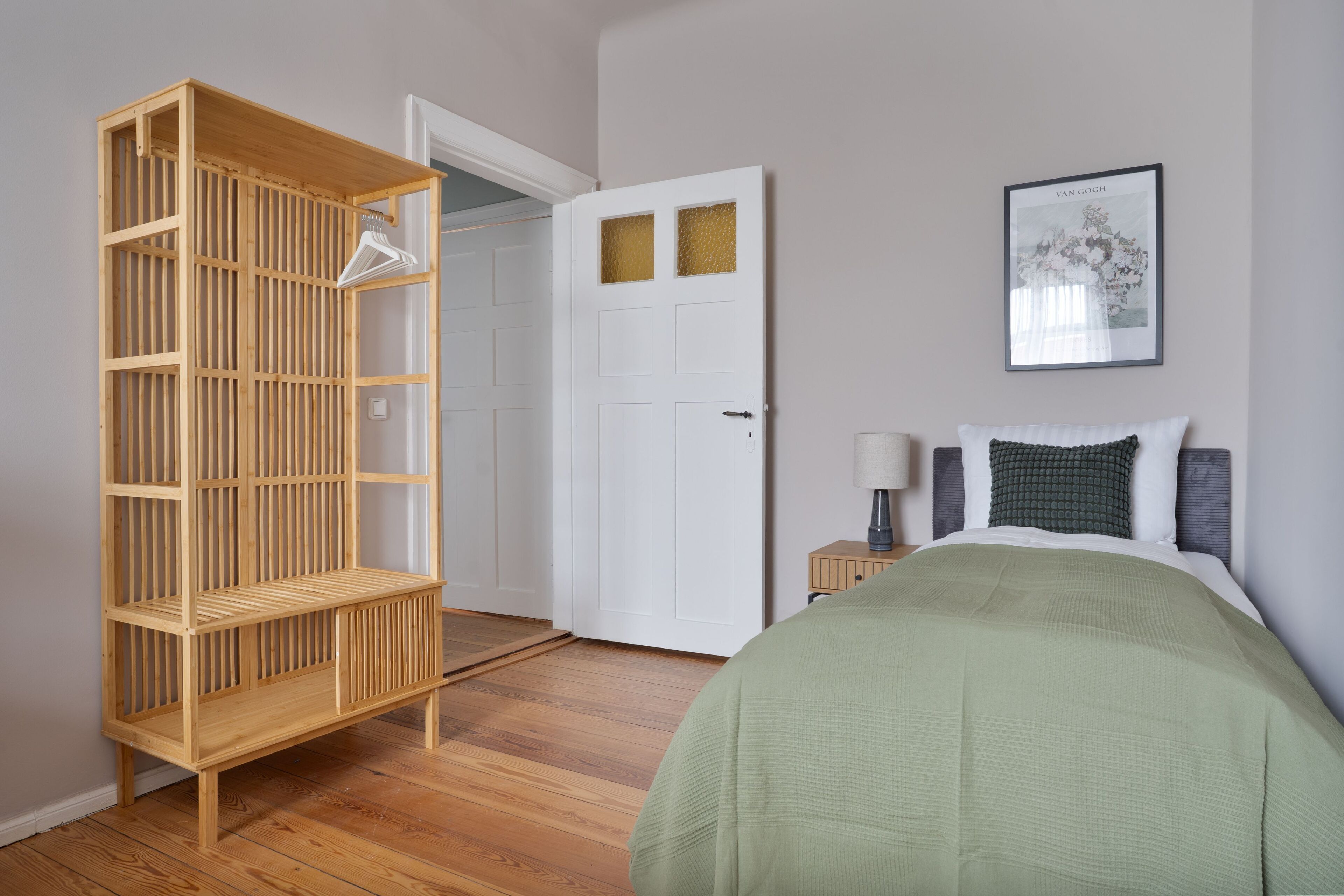 A bedroom with a bed, a nightstand, a wooden wardrobe, and a door.