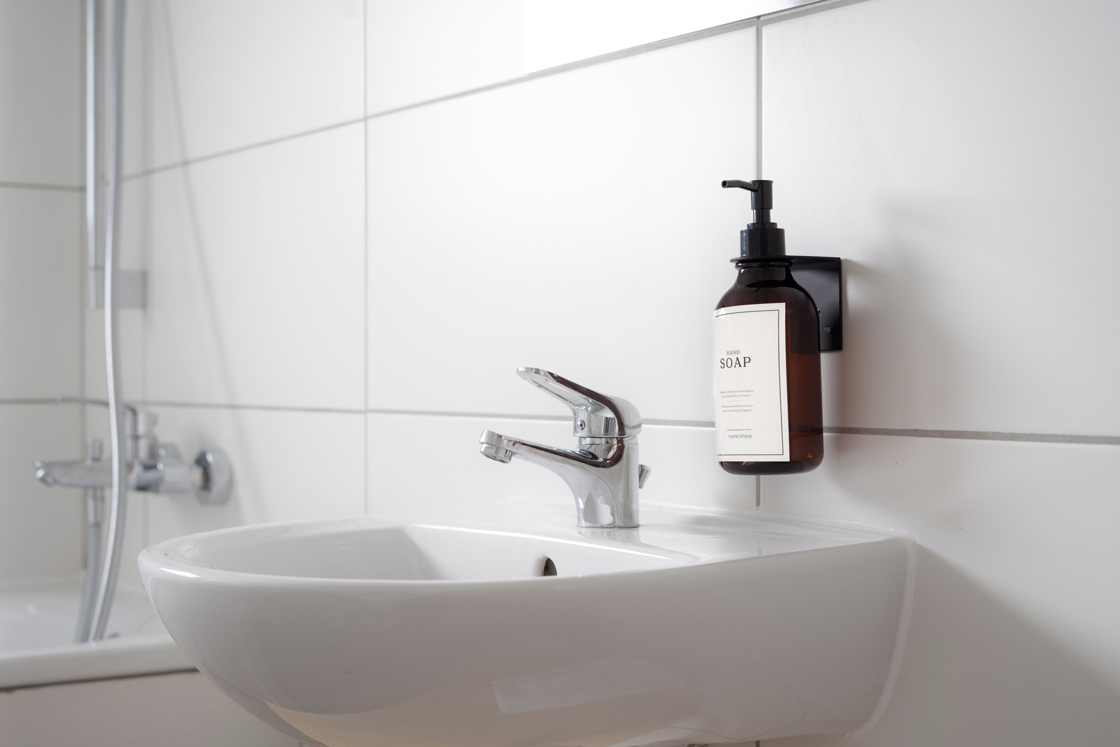 Une salle de bain avec un lavabo blanc, un robinet chromé et un distributeur de savon fixé au mur.