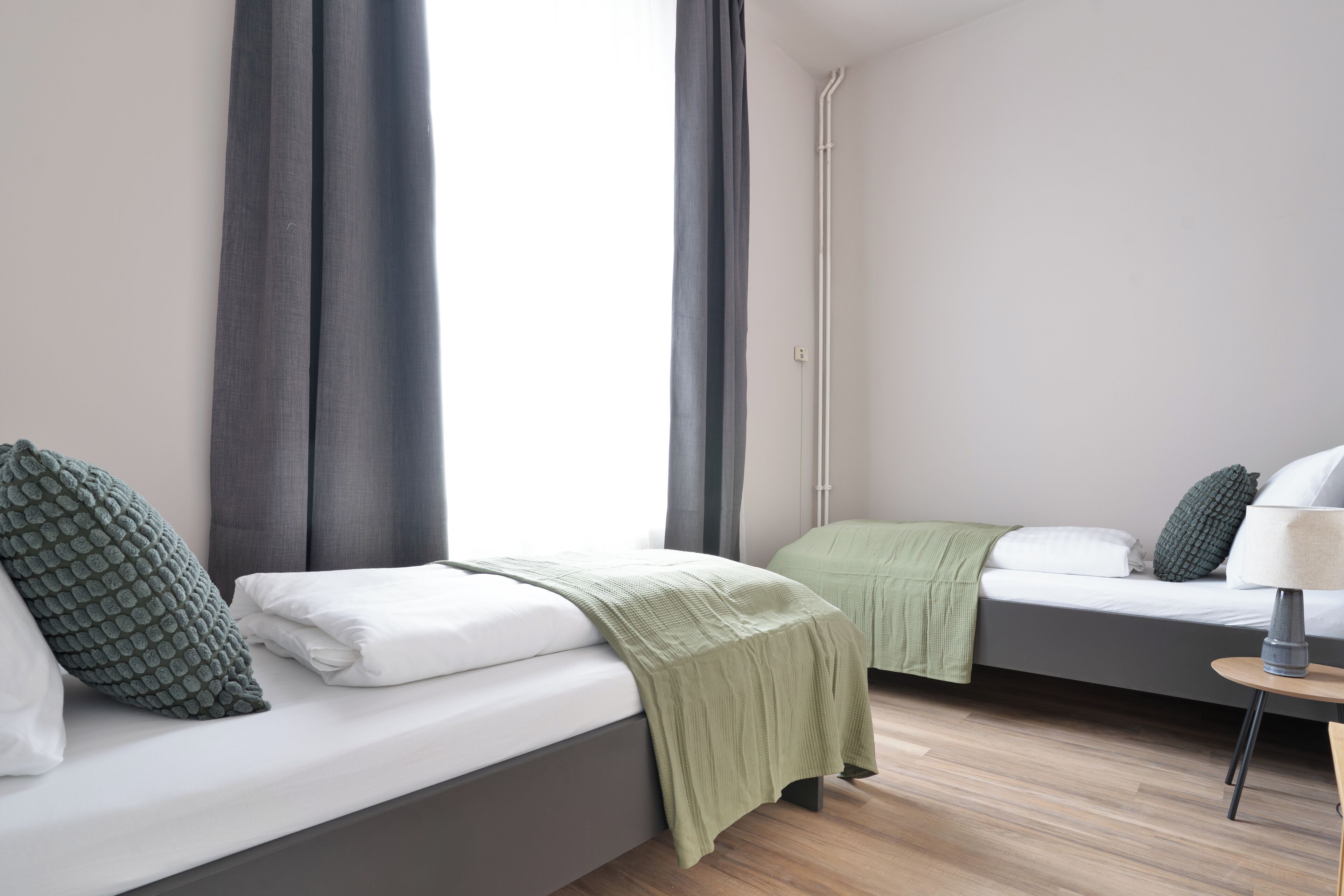 Une chambre d’hôtel moderne, équipée d’un lit, d’une table de chevet avec une lampe et d’une fenêtre avec des rideaux.