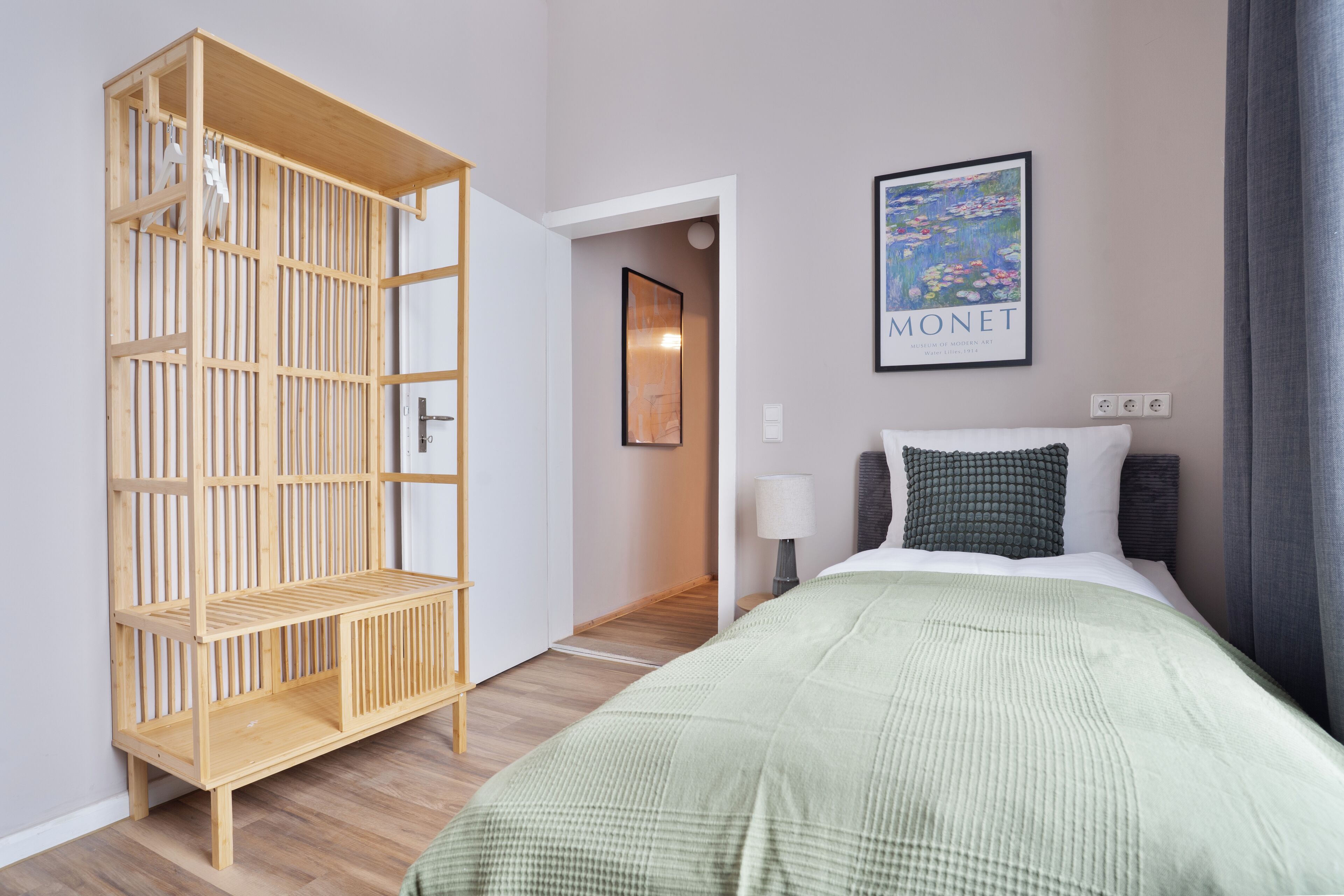 Une chambre d’hôtel avec un lit, une armoire en bois, un tableau encadré et une lampe.